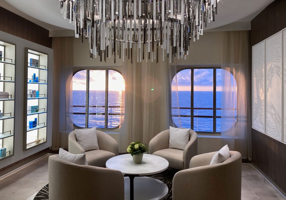 four chairs and a round table seating area looking out windows on a cruise ship