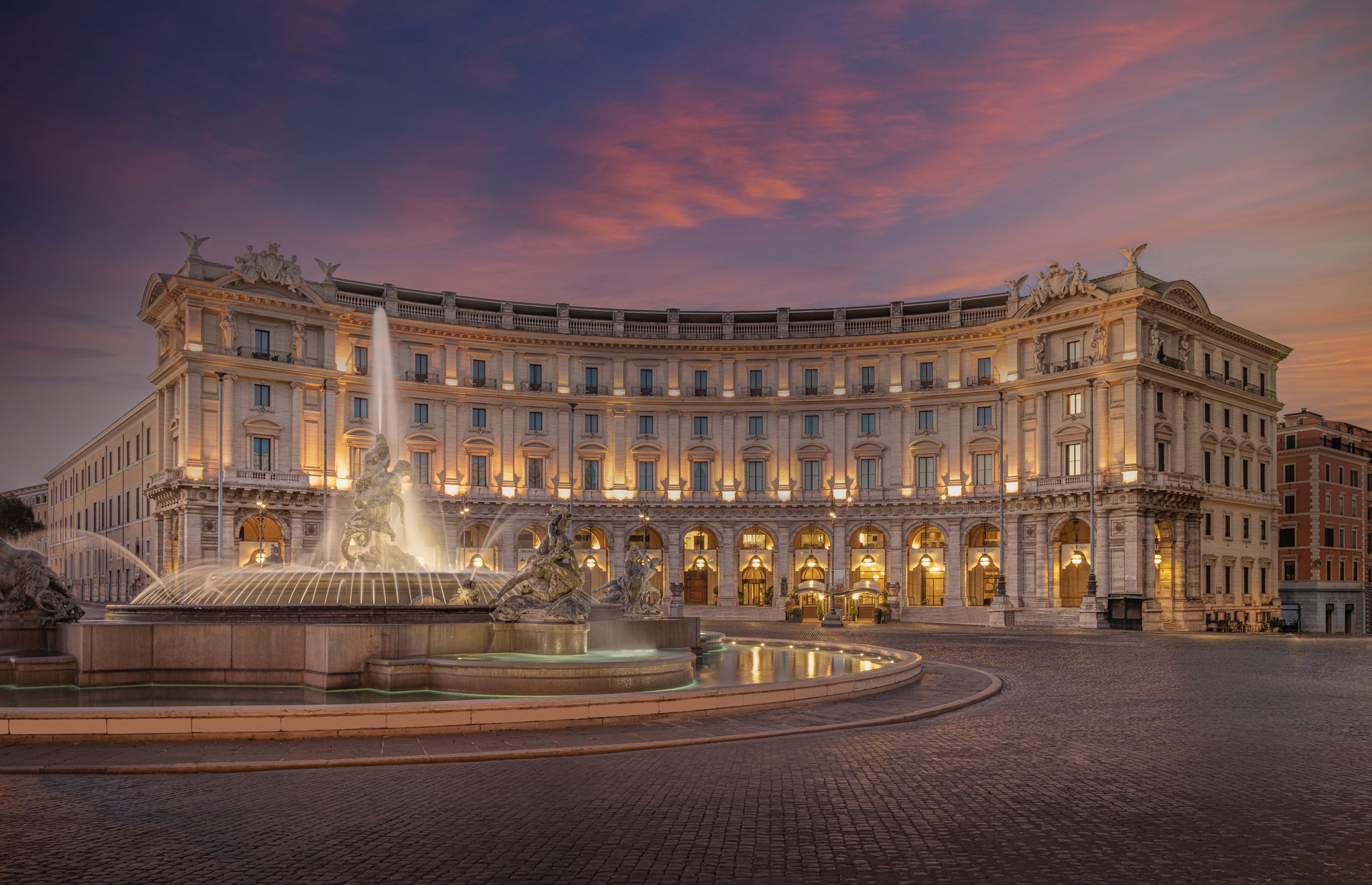 evening sunset of a rounded builidng and a brick common area with a water fountain in the middle